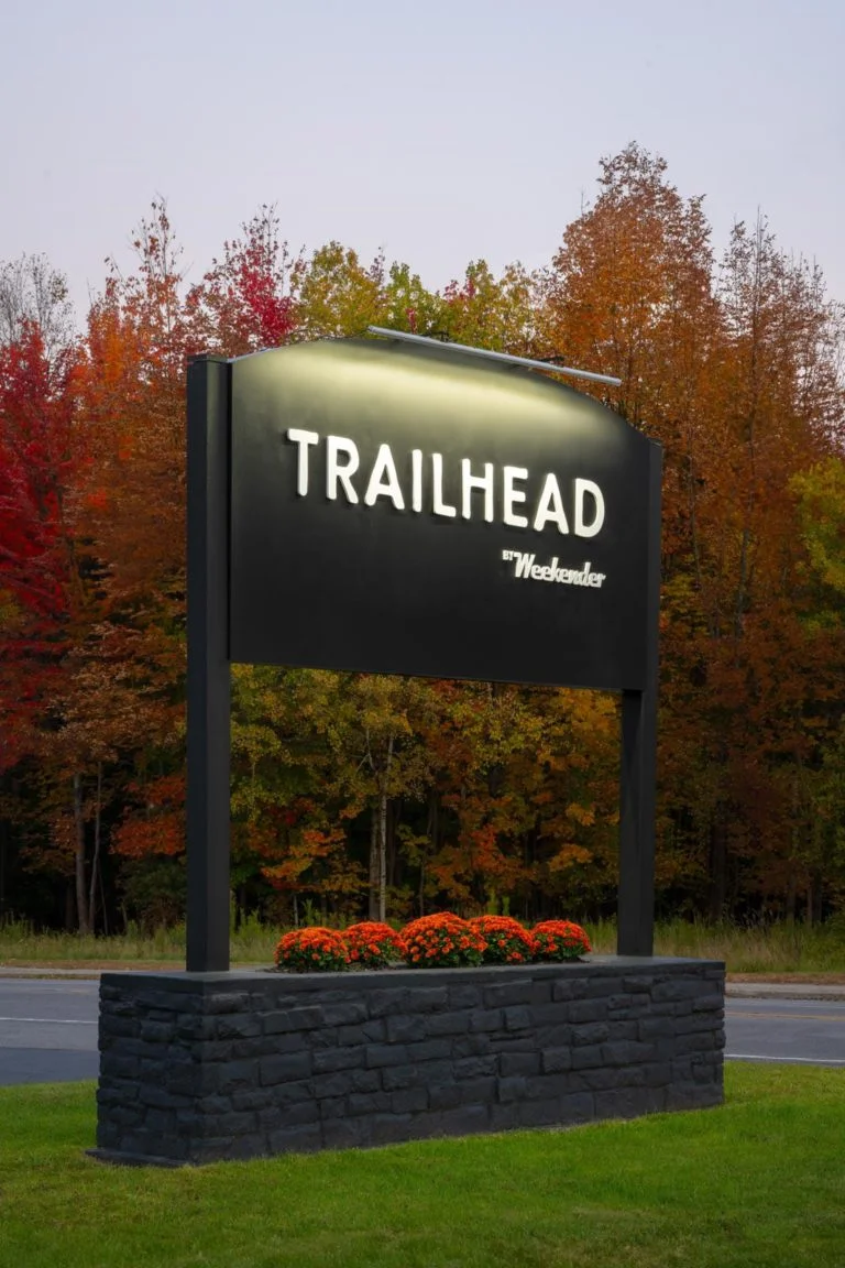 A black sign with the words trailhead in front of trees.