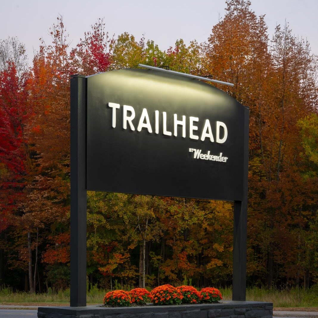 A black sign with the words trailhead in front of trees.