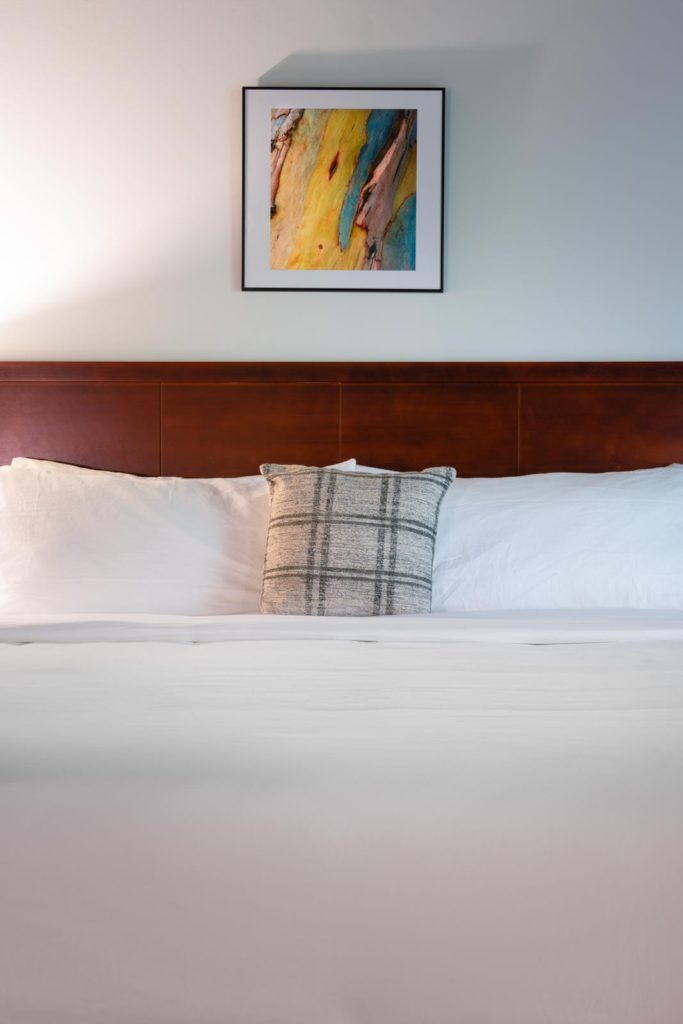 A bed in a hotel room with a painting on the wall.