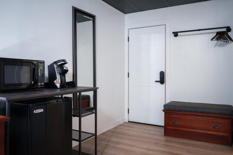 A room with a refrigerator, microwave, and a bench.