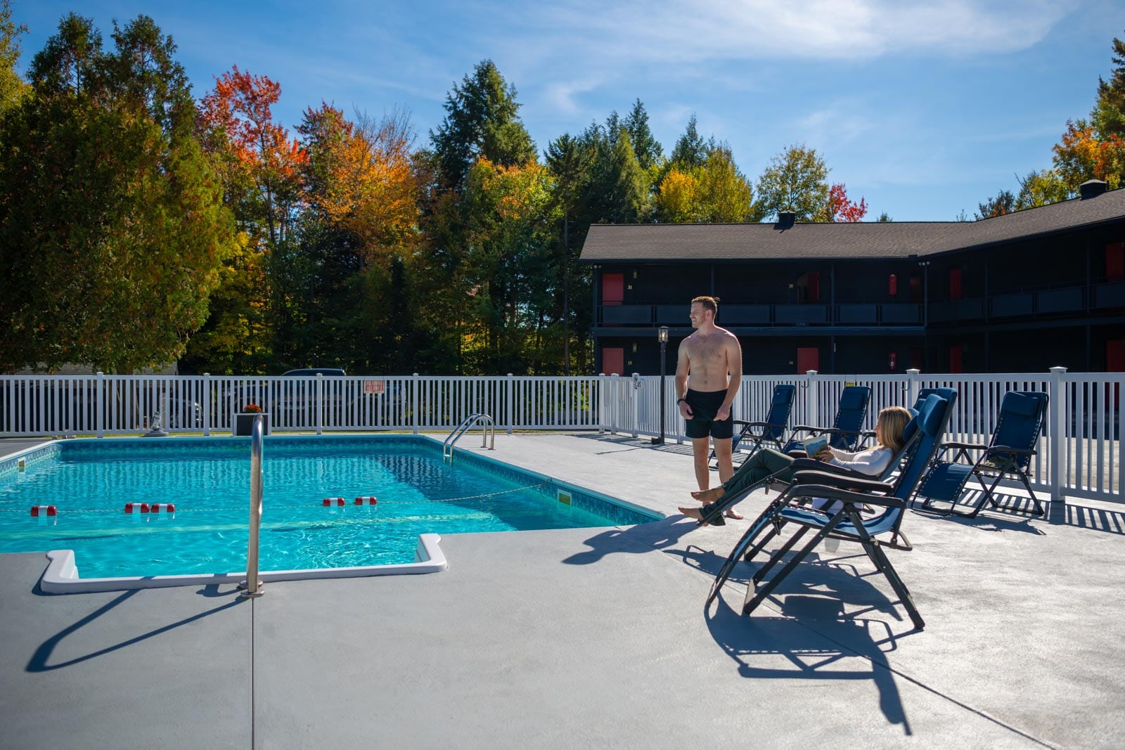 A man is sitting in a lounge chair next to a swimming pool.