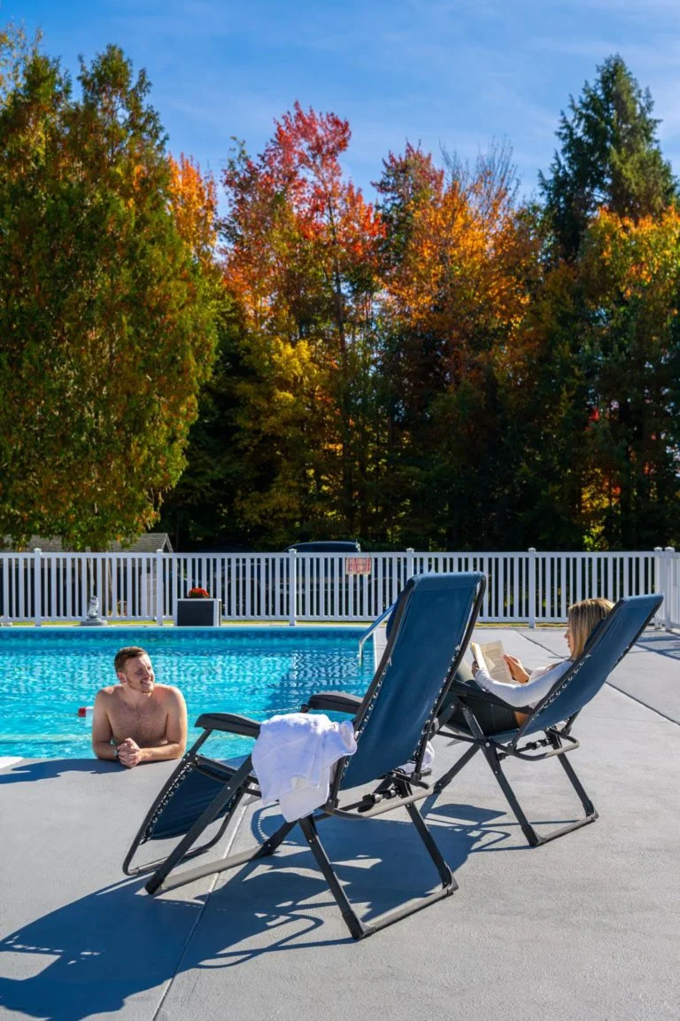 A man and a woman relaxing in a lounge chair by a pool.