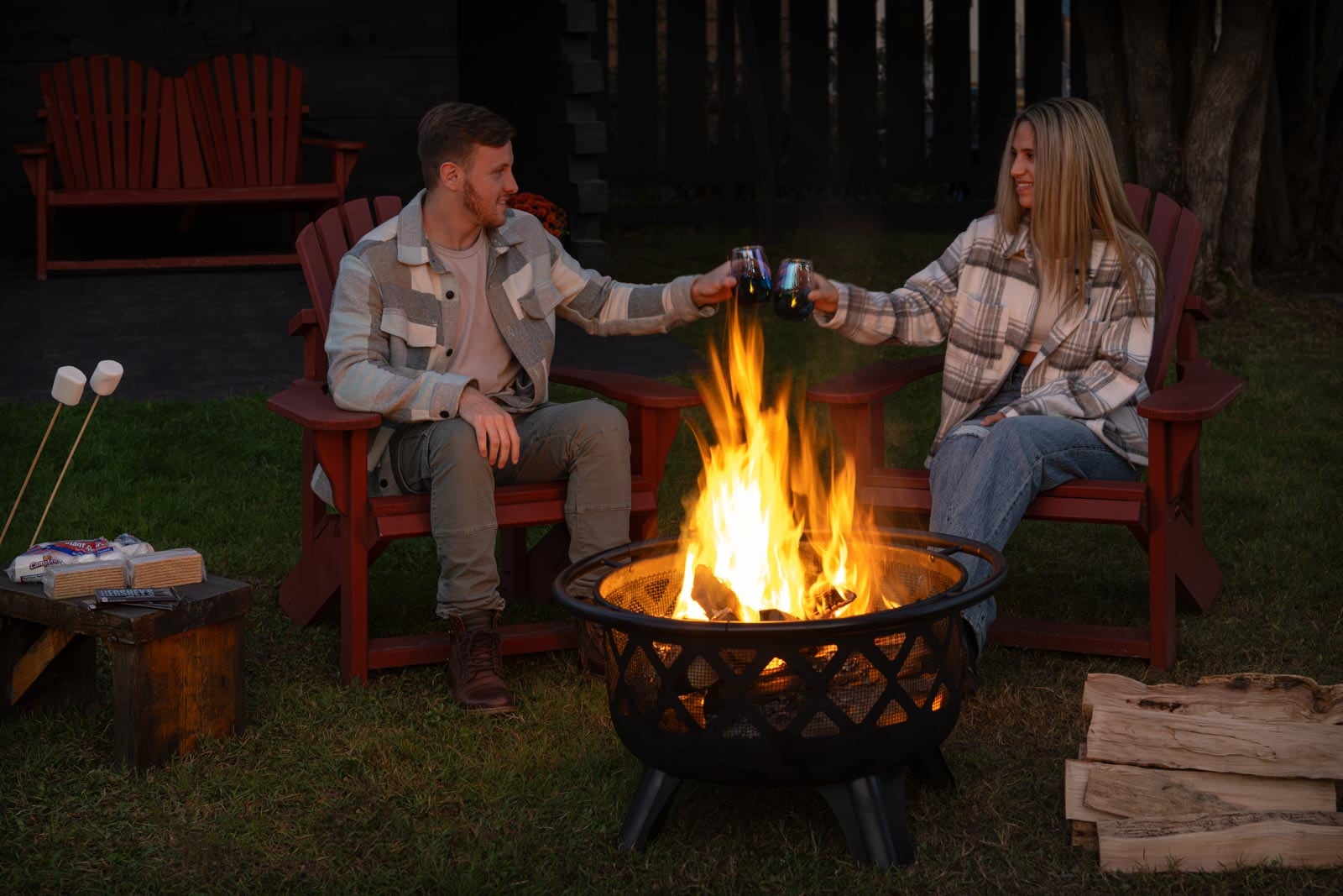 A man and woman sitting in chairs next to a fire pit.